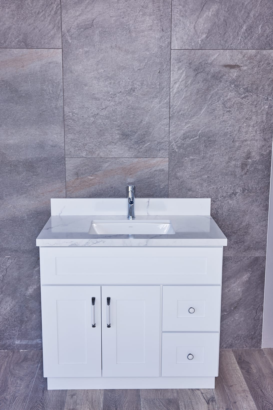 White bathroom vanity with marble countertop against gray stone wall.