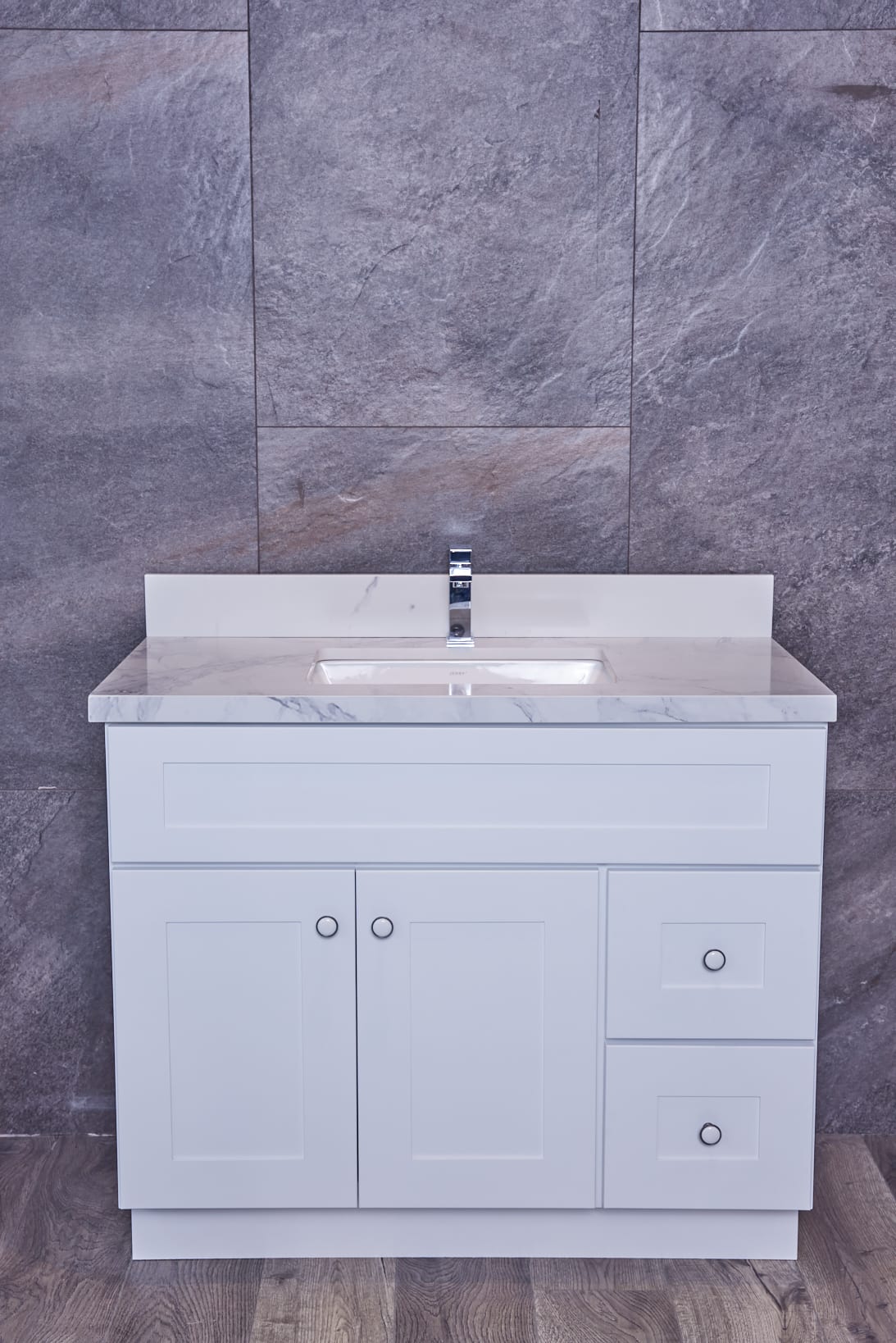 White bathroom vanity with marble countertop against gray stone wall.