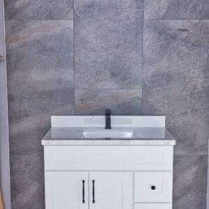 White bathroom vanity with marble countertop against gray tiled wall.