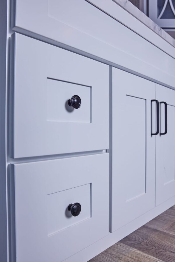 White kitchen cabinet with black handles and knobs on wooden floor.