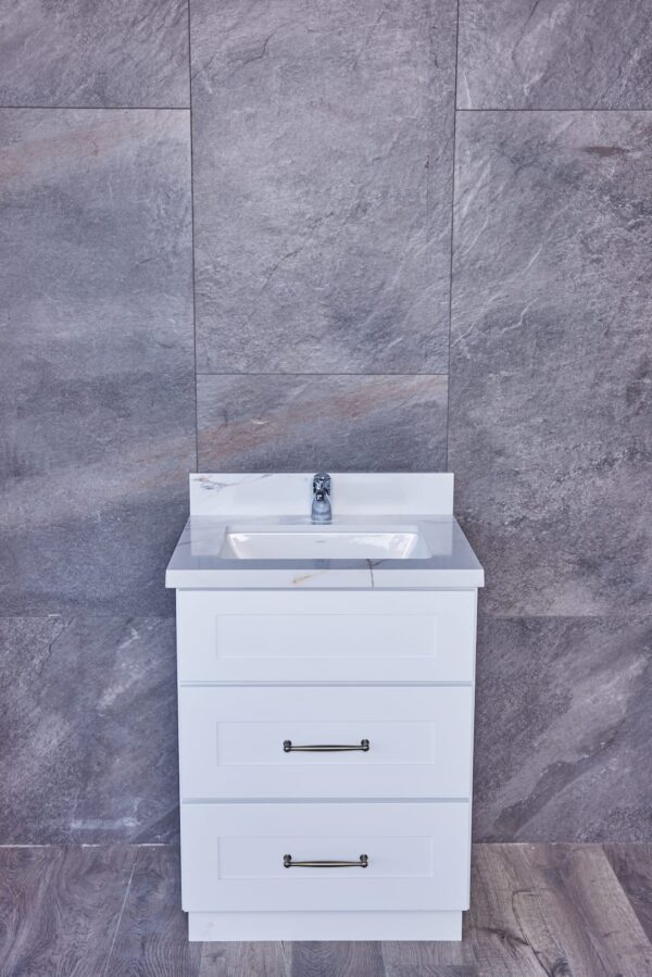 White bathroom vanity with sink against gray tiled wall.