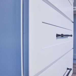 White kitchen drawers with black handles against a blue wall.