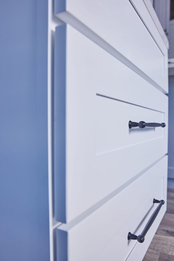 White kitchen drawers with black handles against a blue wall.