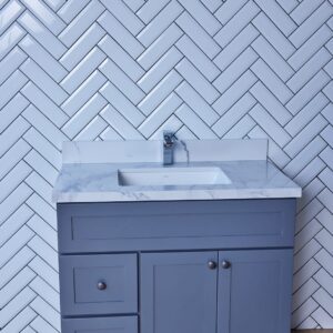 Blue bathroom vanity with marble countertop and herringbone tile backsplash.