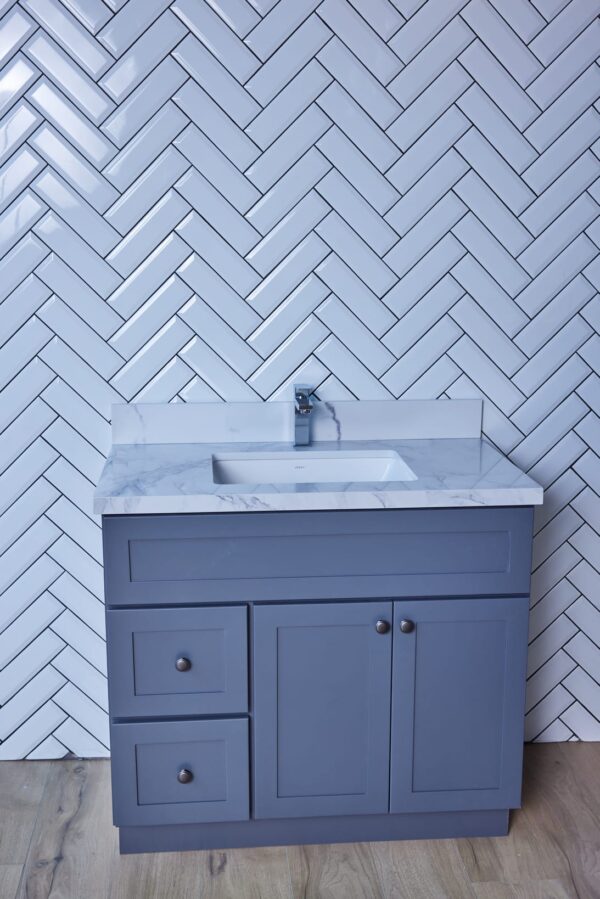 Blue bathroom vanity with marble countertop and herringbone tile backsplash.