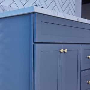 Blue kitchen cabinet with gold knobs and marble countertop.