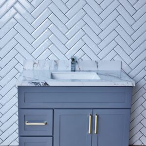 Gray bathroom vanity with marble countertop and herringbone tile backsplash.