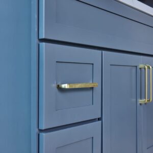 Blue kitchen cabinet with gold handles and marble countertop.