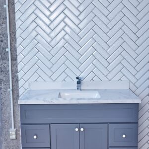 Gray bathroom vanity with marble countertop and herringbone tile backsplash.