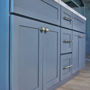 Blue kitchen cabinets with brass handles on wooden floor.