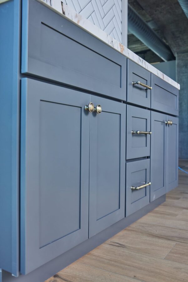 Blue kitchen cabinets with brass handles on wooden floor.