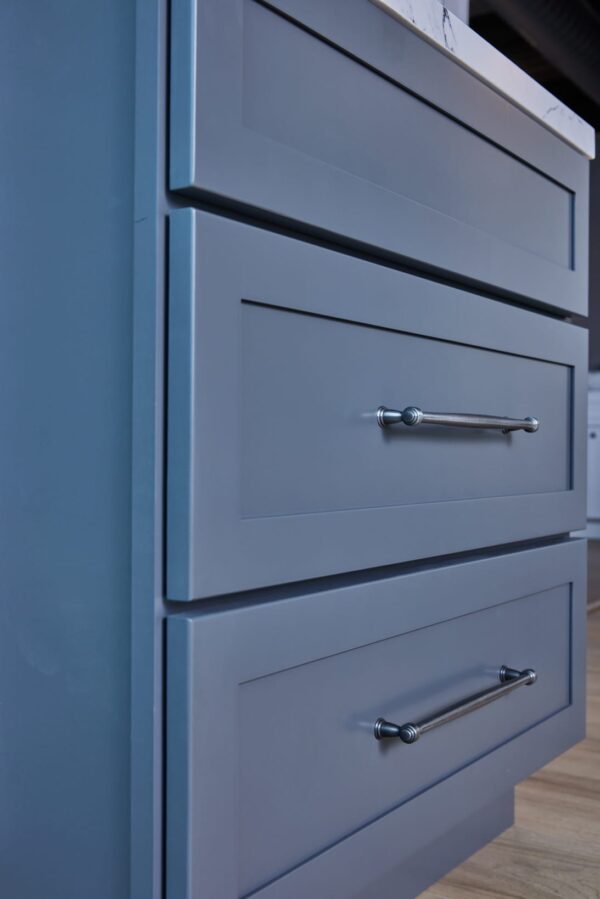 Blue kitchen cabinets with silver handles and marble countertop.