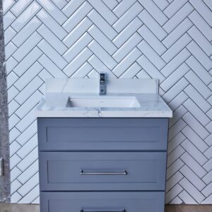 Gray bathroom vanity with white sink against herringbone tile wall.