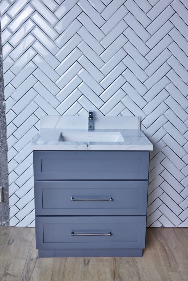 Gray bathroom vanity with white sink against herringbone tile wall.