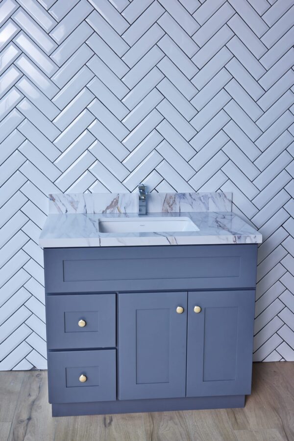 Gray bathroom vanity with marble countertop against herringbone tile wall.