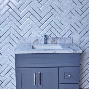 Gray bathroom vanity with marble countertop and herringbone tile backsplash.
