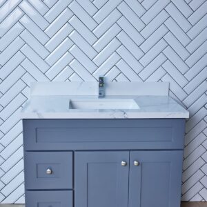 Gray bathroom vanity with marble countertop against herringbone tile wall.
