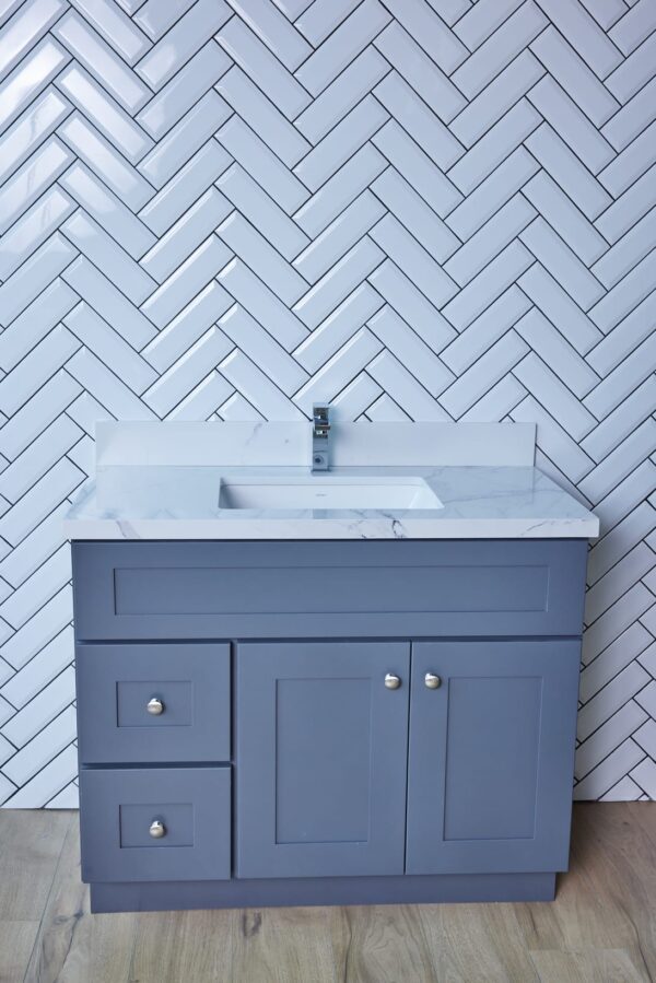 Gray bathroom vanity with marble countertop against herringbone tile wall.