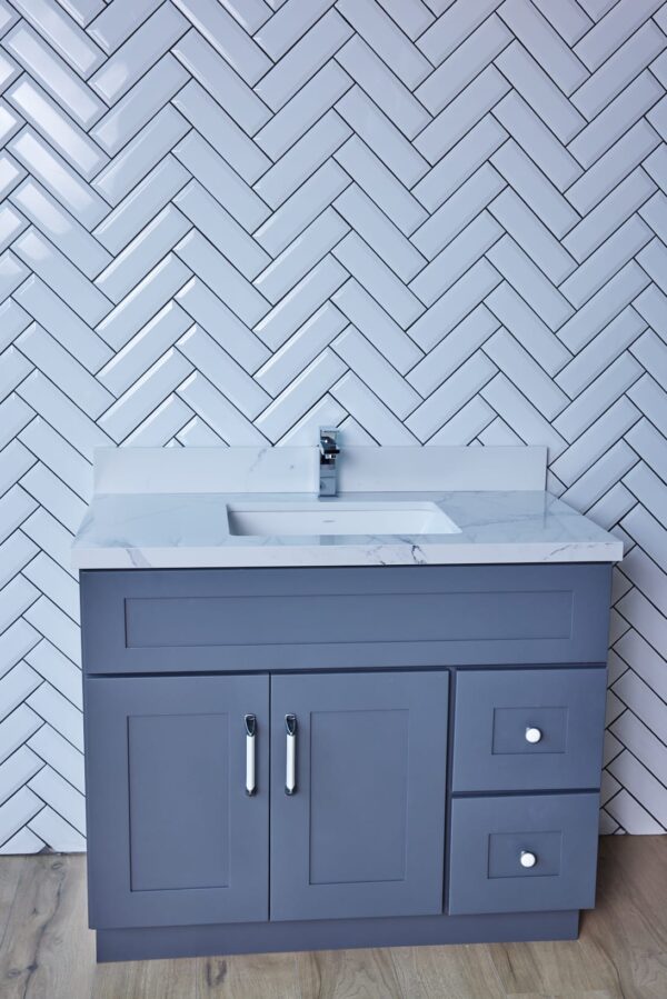 Gray bathroom vanity with marble countertop and herringbone tile backsplash.
