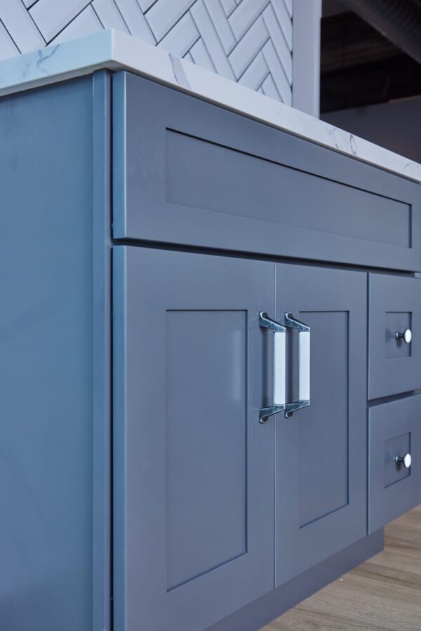 Blue kitchen cabinet with marble countertop and herringbone backsplash.