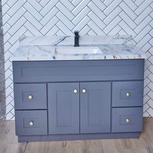 Gray bathroom vanity with marble countertop and herringbone tile backsplash.
