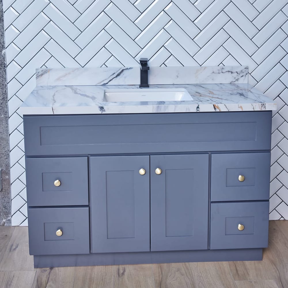 Gray bathroom vanity with marble countertop and herringbone tile backsplash.