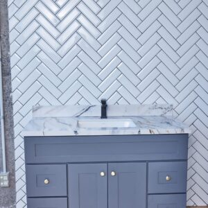 Gray bathroom vanity with marble countertop and herringbone tile backsplash.
