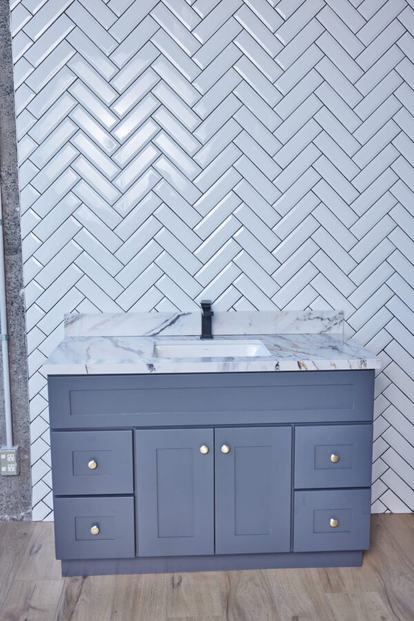 Gray bathroom vanity with marble countertop and herringbone tile backsplash.