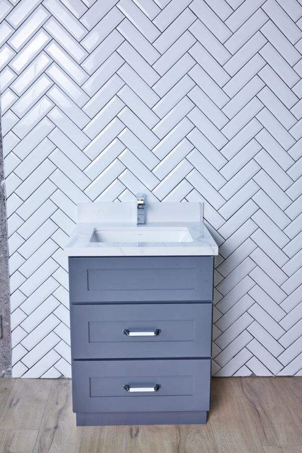Gray bathroom vanity against white herringbone tile wall.