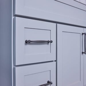 Light gray kitchen cabinet with marble countertop and black handles.