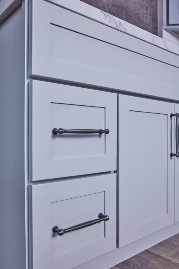 Light gray kitchen cabinet with marble countertop and black handles.