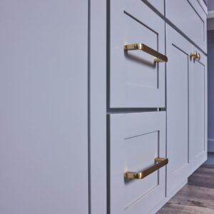 White kitchen cabinets with gold handles on wooden floor.