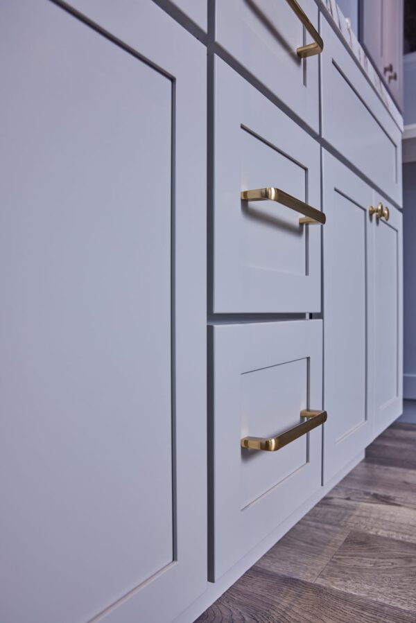 White kitchen cabinets with gold handles on wooden floor.