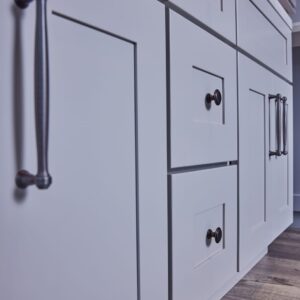 White kitchen cabinets with black handles on wooden floor.