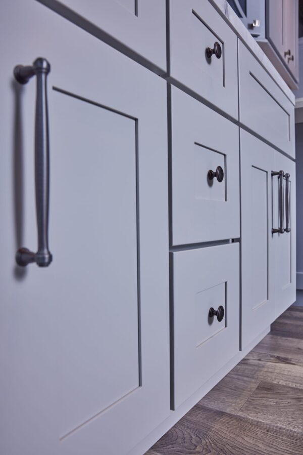 White kitchen cabinets with black handles on wooden floor.