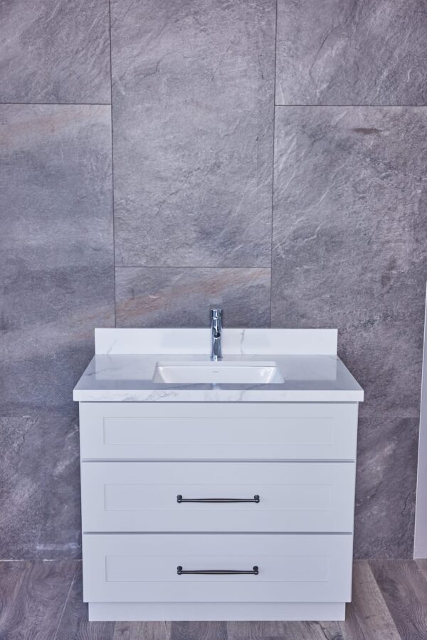 White bathroom vanity with marble countertop against gray tiled wall.