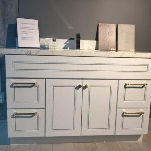 White kitchen cabinet with marble countertop and brass handles.