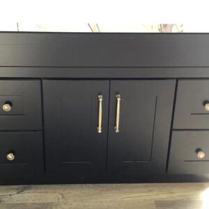 Black kitchen cabinet with silver handles on a wooden floor.