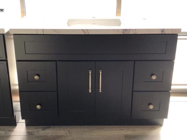 Black kitchen cabinet with marble countertop and brass handles.