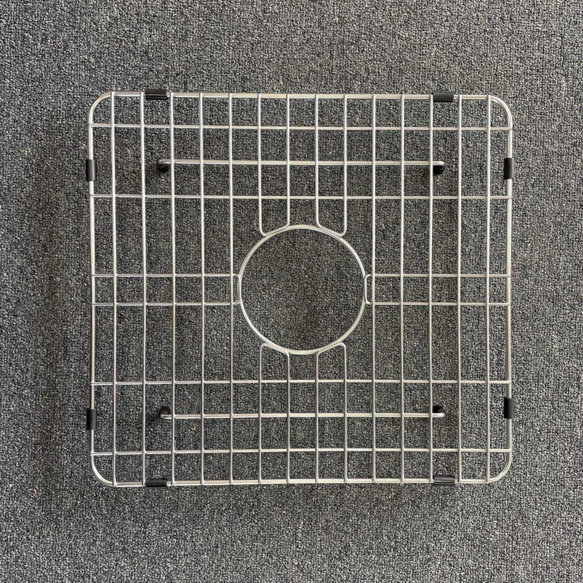 Square metal sink grid on a gray carpet background.