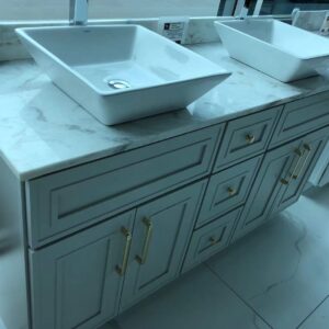 Light grey kitchen cabinet with marble countertop and two sinks.
