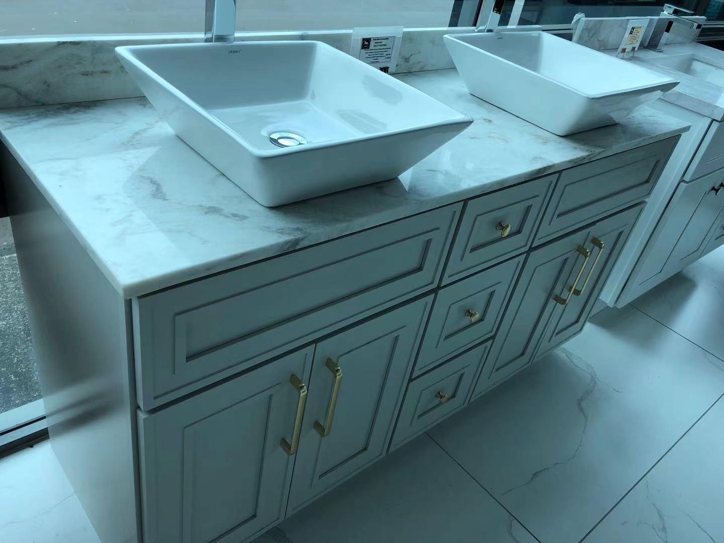 Light grey kitchen cabinet with marble countertop and two sinks.