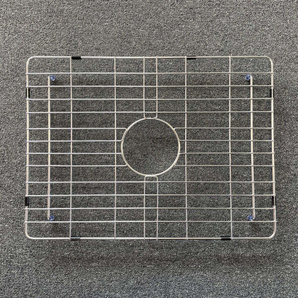 Stainless steel sink grid on a textured surface.
