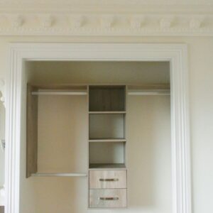 Elegant open wardrobe with shelves and drawers, featuring ornate ceiling moldings.