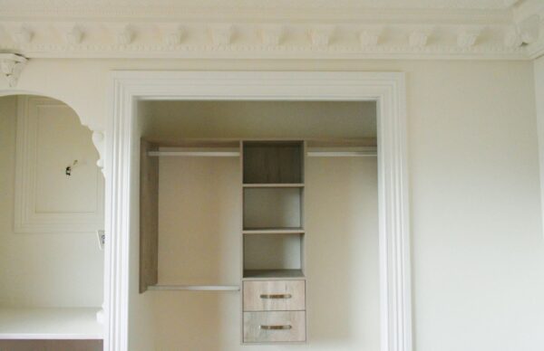 Elegant open wardrobe with shelves and drawers, featuring ornate ceiling moldings.