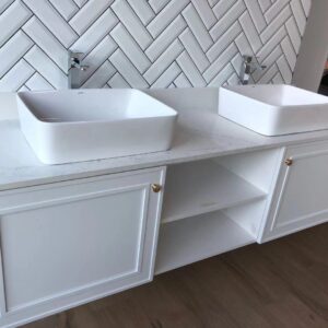 Modern white bathroom vanity with two sinks and herringbone tile backsplash.
