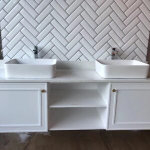 White double sink vanity with herringbone tile backsplash.