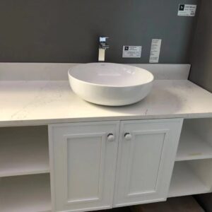 White bathroom vanity with round basin and faucet against gray wall.