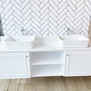 Wooden bathroom vanity with marble countertop and herringbone tile backsplash.