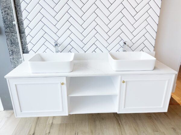 Wooden bathroom vanity with marble countertop and herringbone tile backsplash.
